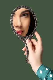 Image of Beautiful woman looking in handheld mirror on dark green background, closeup