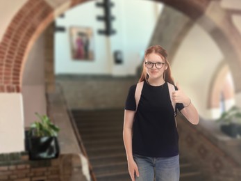 Image of Teenage student with eyeglasses and backpack showing thumbs-up gesture in college