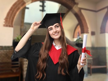 Image of Happy student in academic dress holding diploma after graduation in university