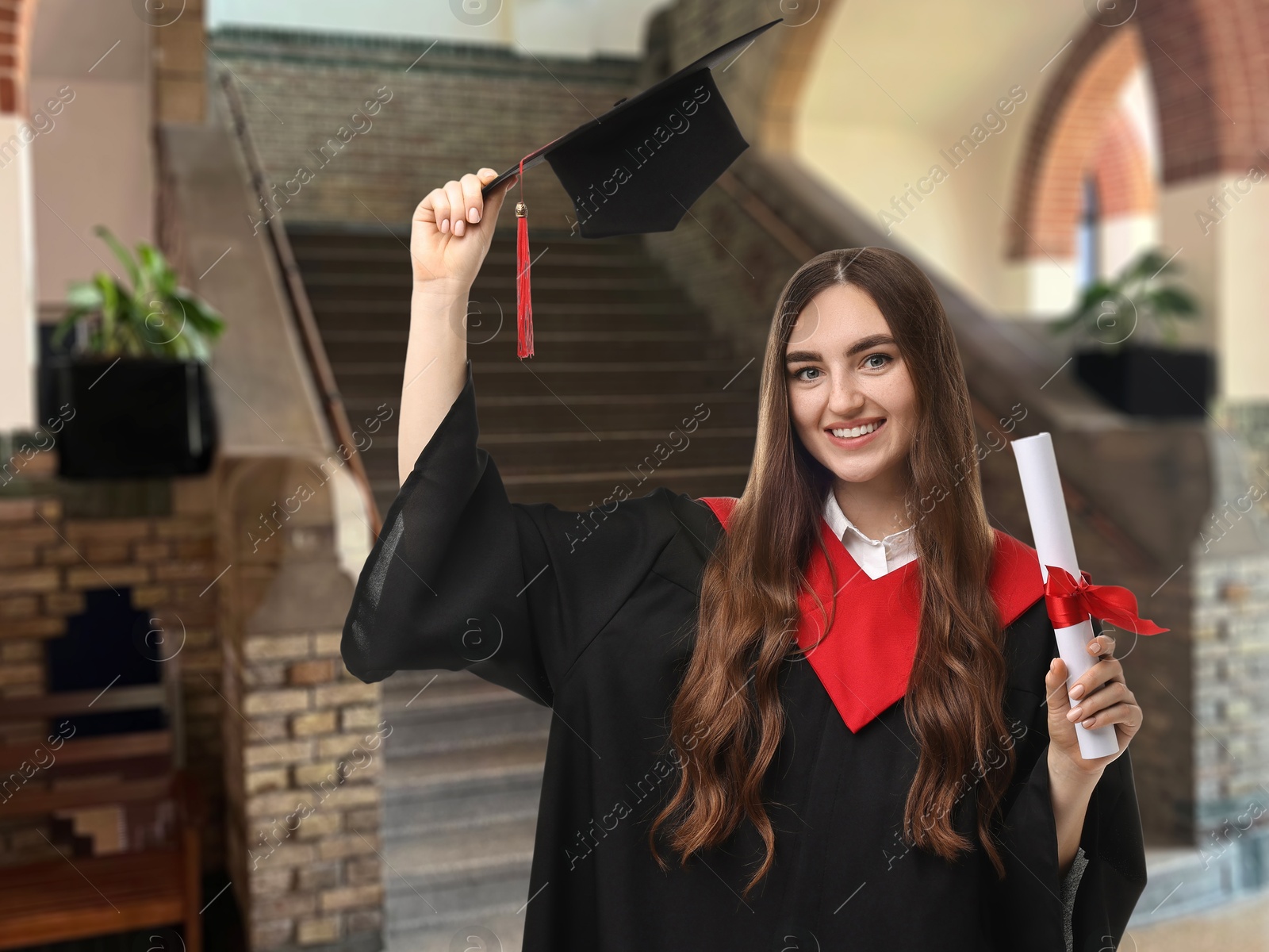 Image of Happy student in academic dress holding diploma after graduation in university