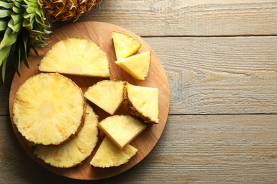 Photo of Slices of ripe pineapple on wooden table, top view. Space for text