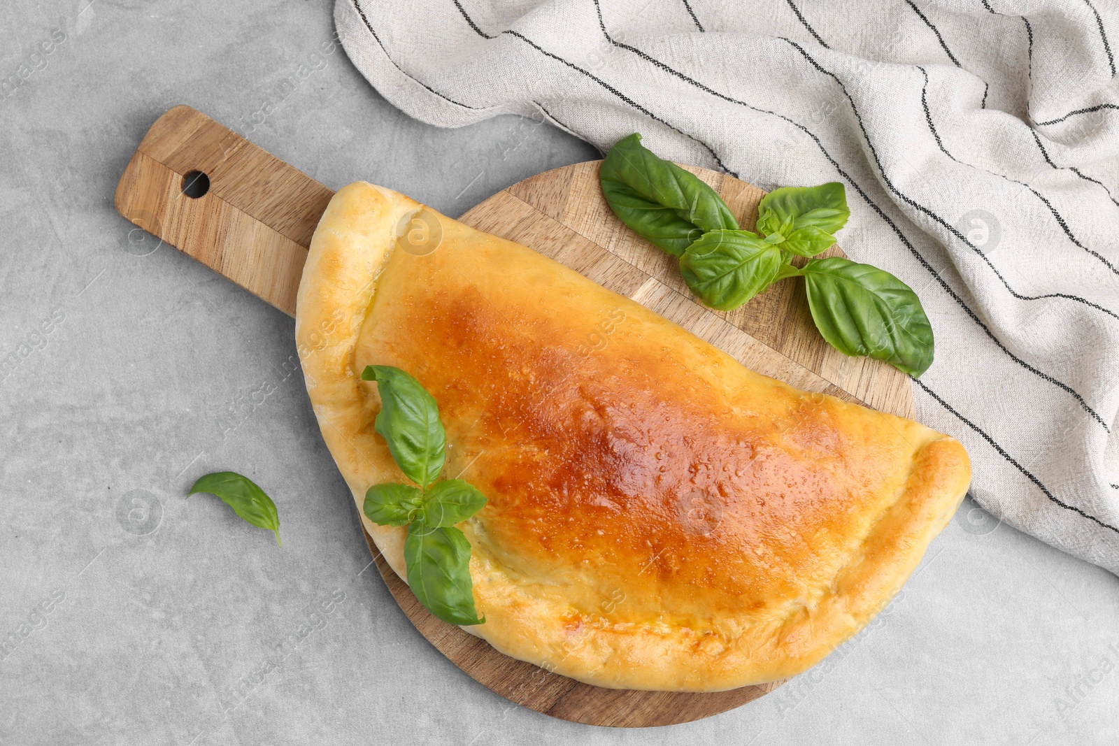 Photo of Tasty vegetarian calzone with basil on grey table, top view