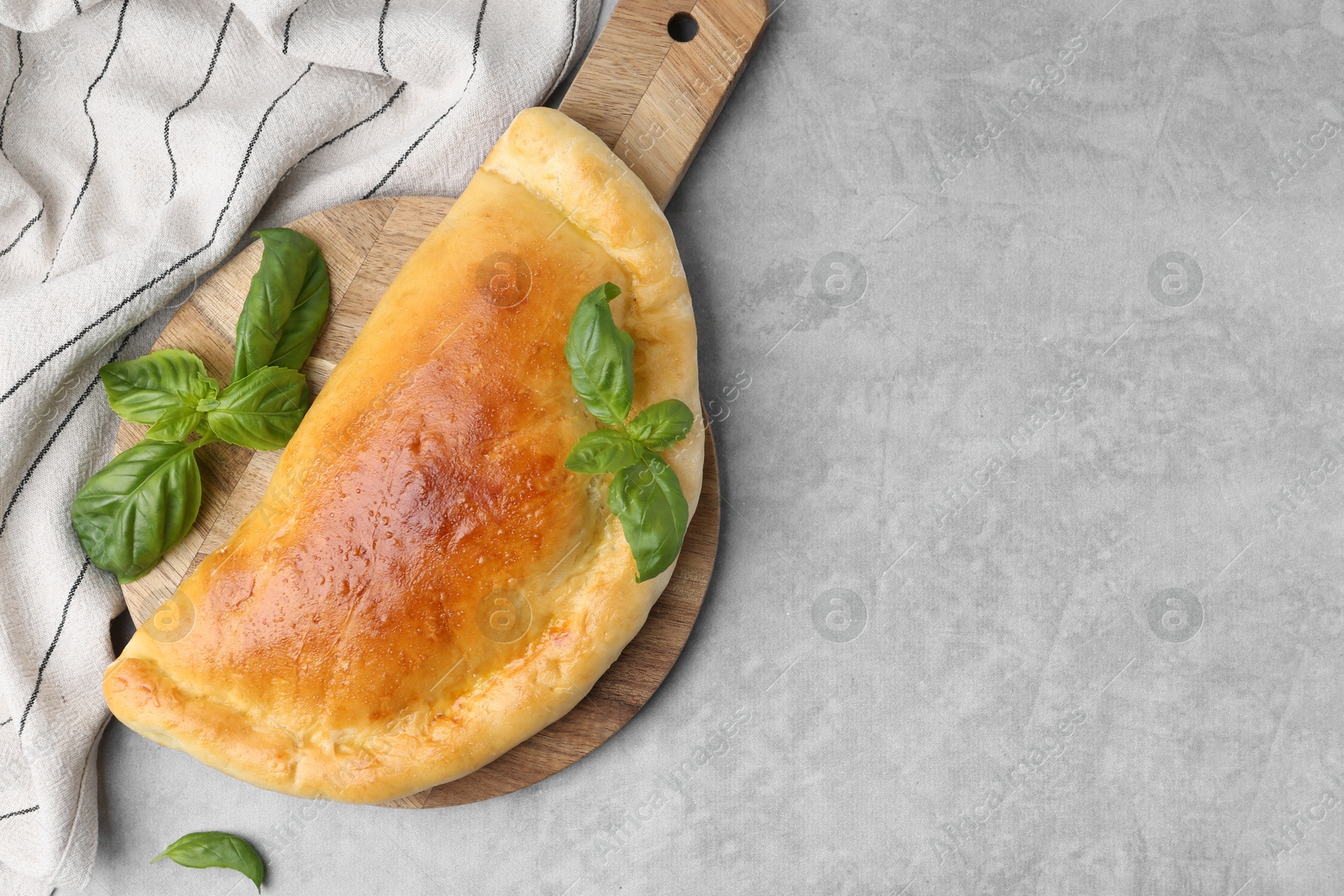 Photo of Tasty vegetarian calzone with basil on grey table, top view. Space for text