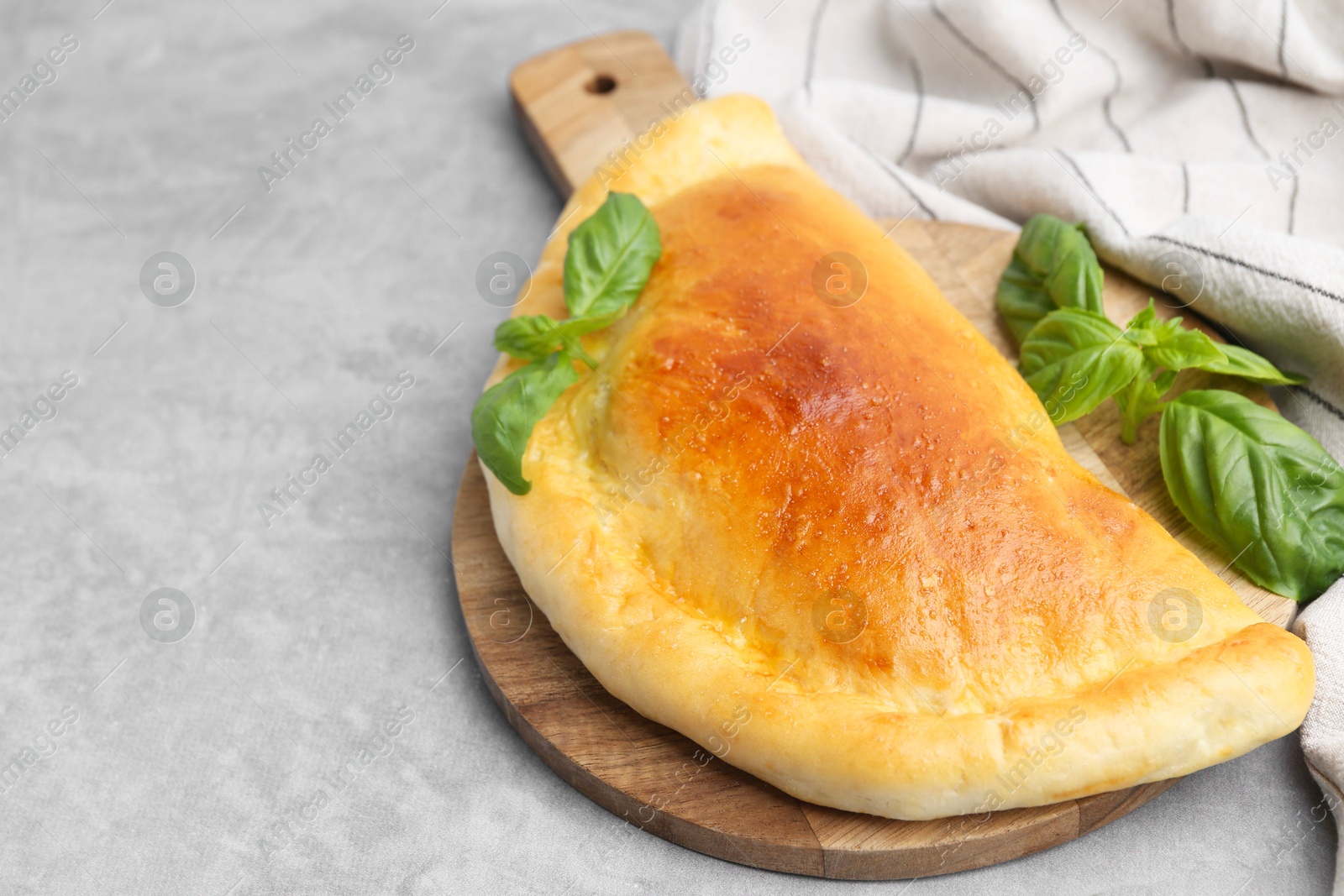 Photo of Tasty vegetarian calzone with basil on grey table, closeup. Space for text