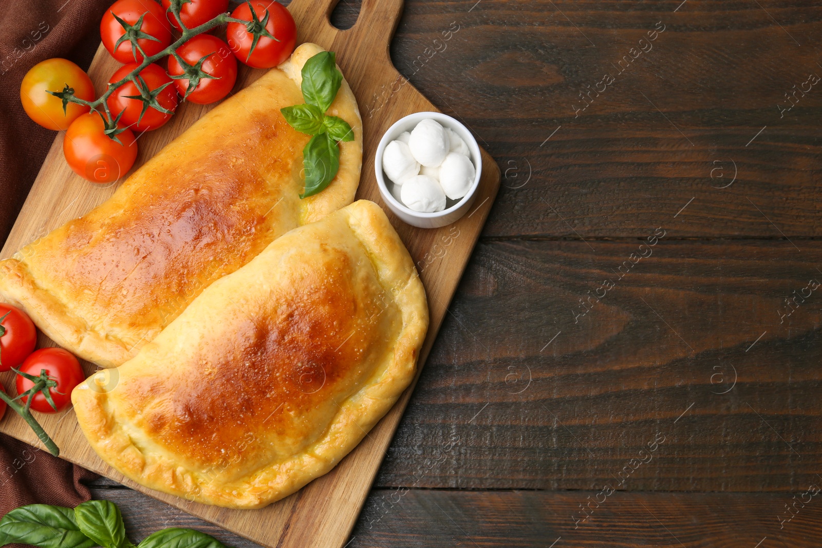 Photo of Tasty vegetarian calzones with basil, mozzarella cheese and tomatoes on wooden table, top view. Space for text