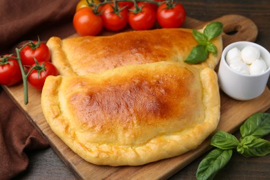 Photo of Tasty vegetarian calzones with basil, mozzarella cheese and tomatoes on wooden table, closeup