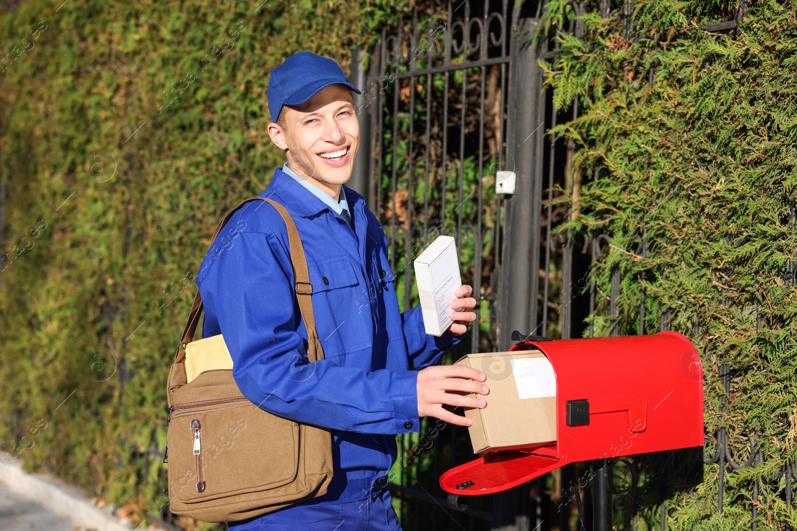 Photo of Postman putting parcel into mail box outdoors