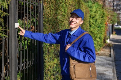 Photo of Postman with bag ringing entrance bell outdoors