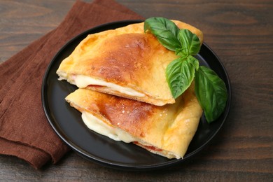 Photo of Pieces of delicious calzone pizza with mozzarella, tomatoes and basil on wooden table, closeup