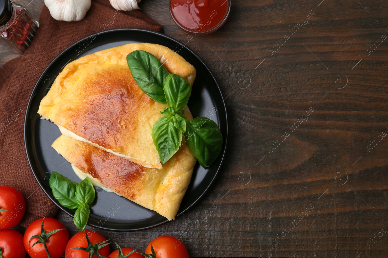 Photo of Pieces of delicious calzone pizza with mozzarella, tomatoes and basil on wooden table, flat lay. Space for text