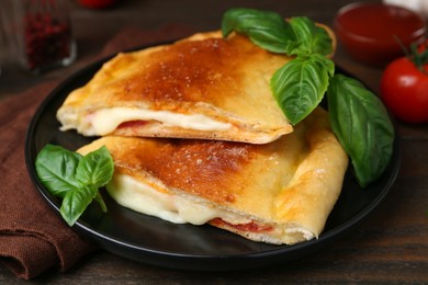 Photo of Pieces of delicious calzone pizza with mozzarella, tomatoes and basil on wooden table, closeup