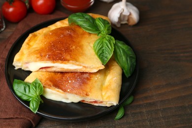 Photo of Pieces of delicious calzone pizza with mozzarella, tomatoes and basil on wooden table, closeup