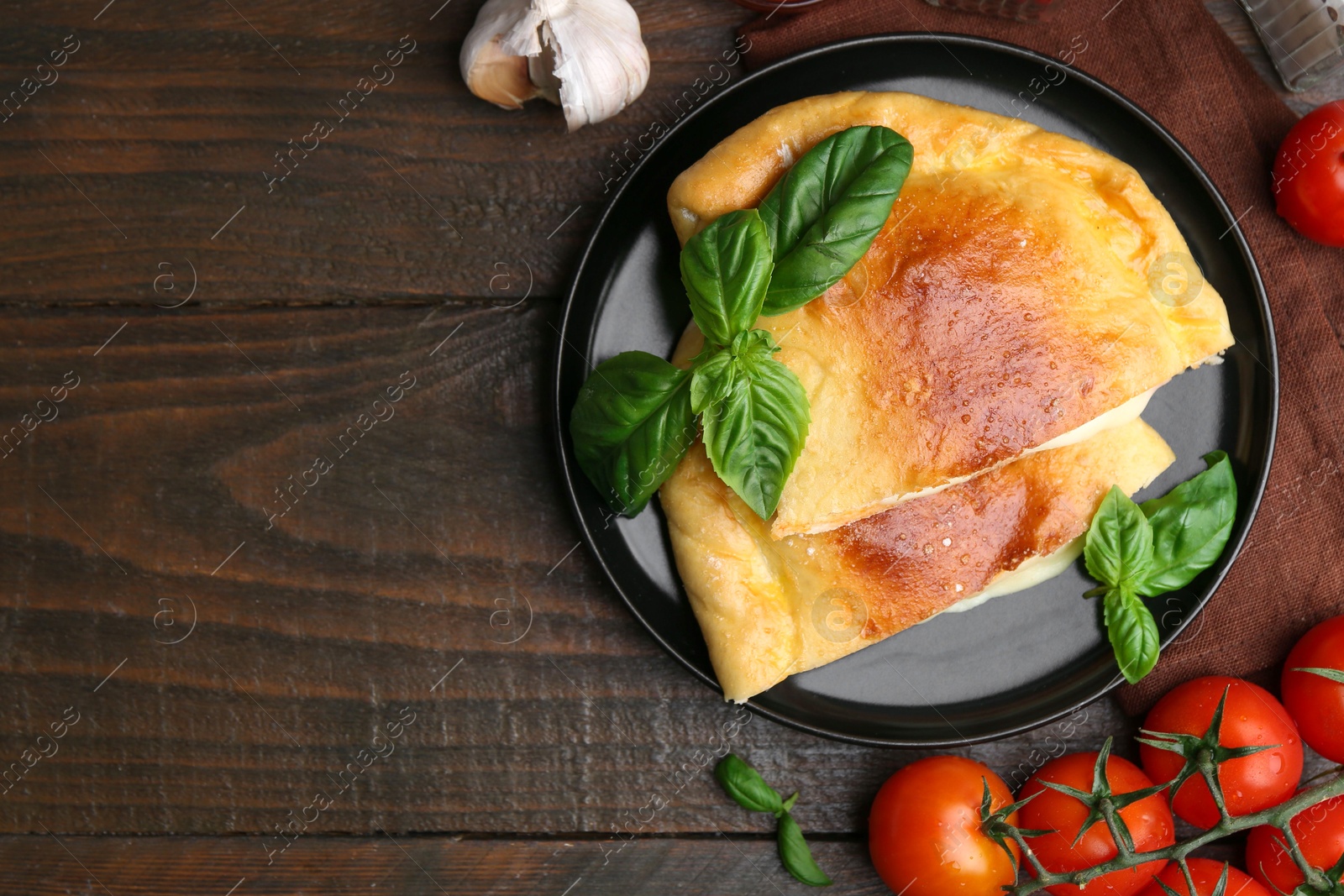 Photo of Pieces of delicious calzone pizza with mozzarella, tomatoes and basil on wooden table, flat lay. Space for text