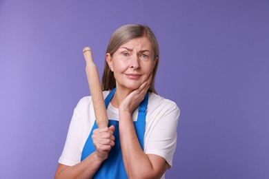 Photo of Emotional woman with rolling pin on violet background