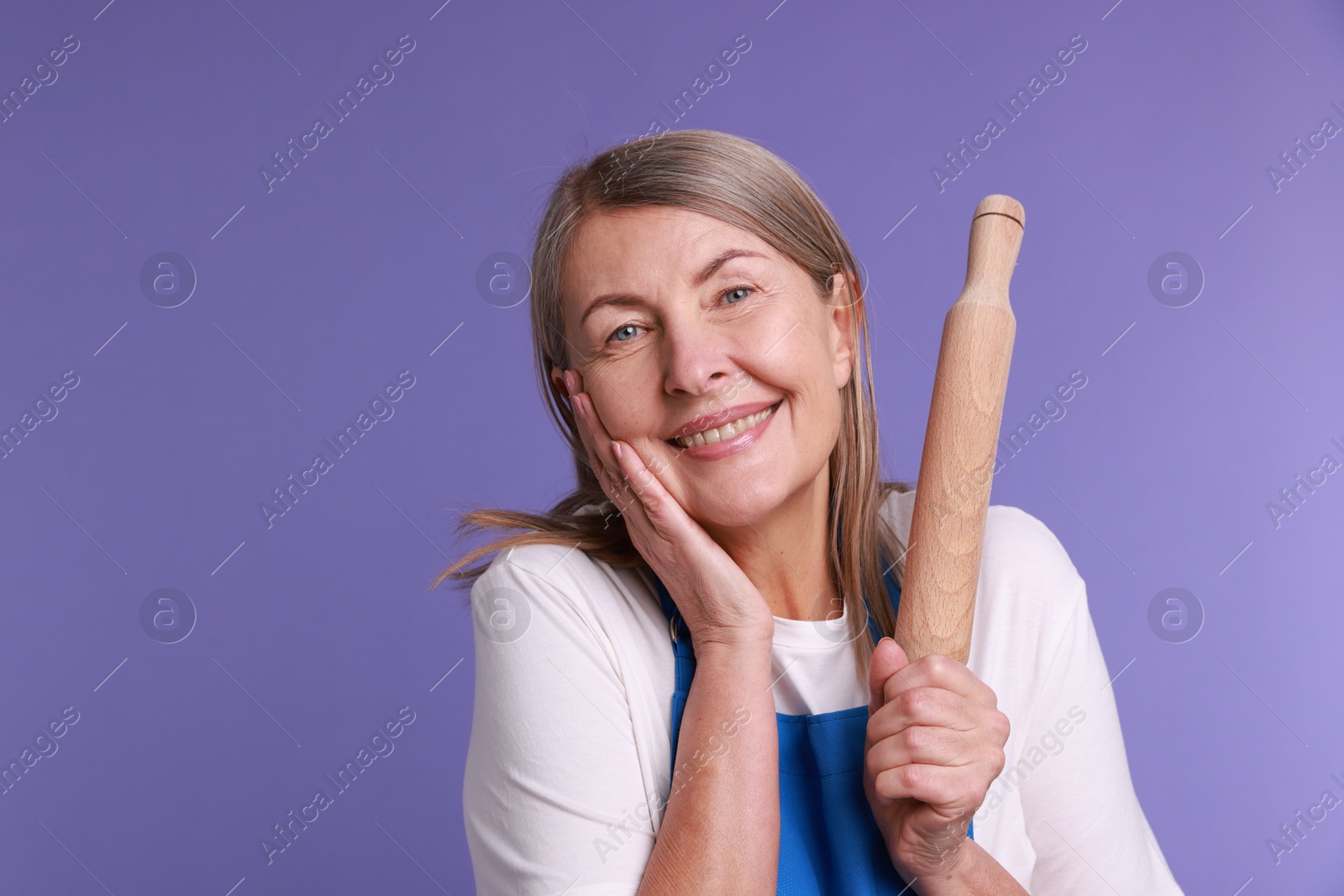 Photo of Happy woman with rolling pin on violet background. Space for text