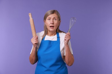 Photo of Surprised woman with rolling pin and whisk on violet background