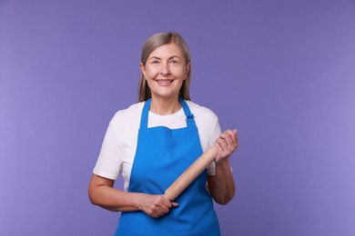 Photo of Happy woman with rolling pin on violet background