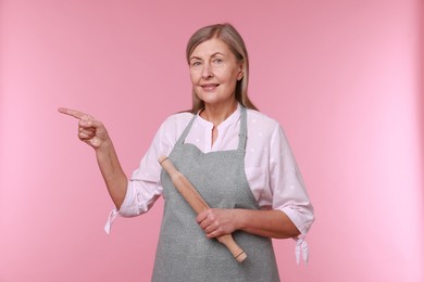 Photo of Happy woman with rolling pin pointing at something on pink background