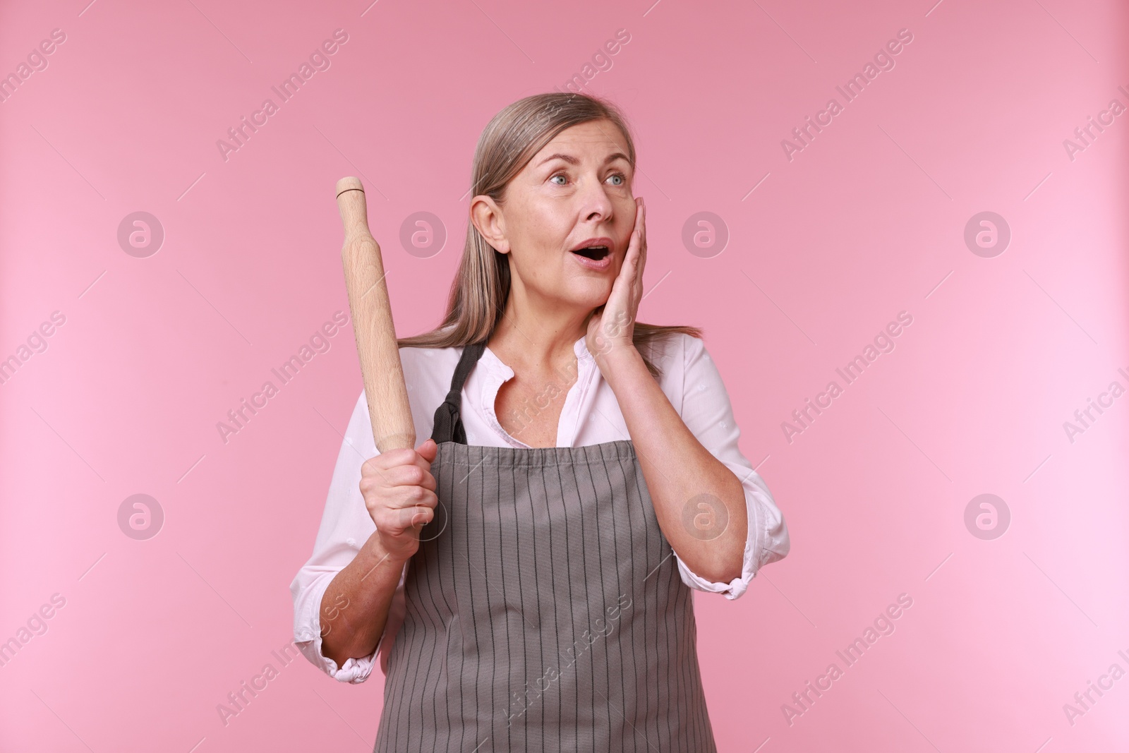 Photo of Emotional woman with rolling pin on pink background