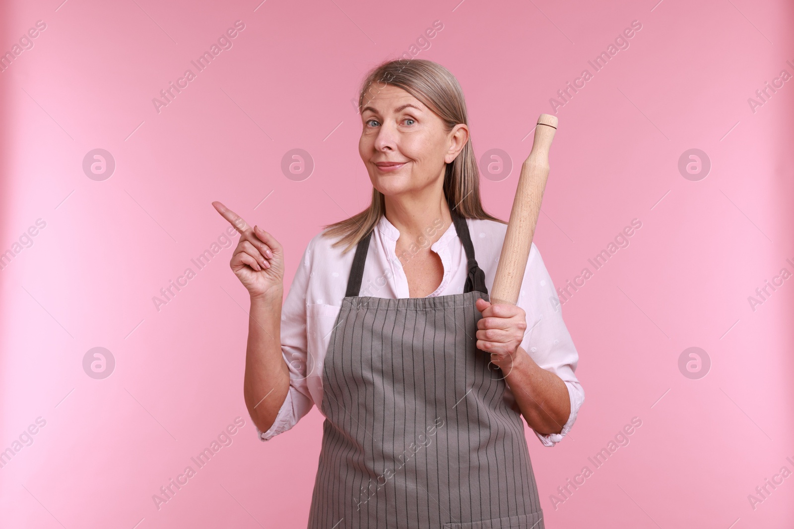 Photo of Woman with rolling pin pointing at something on pink background