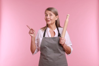 Photo of Woman with rolling pin pointing at something on pink background