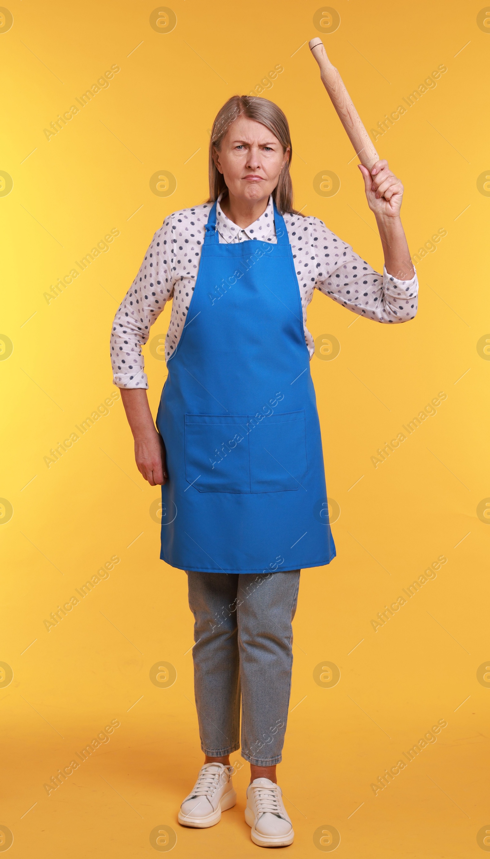 Photo of Angry woman with rolling pin on yellow background