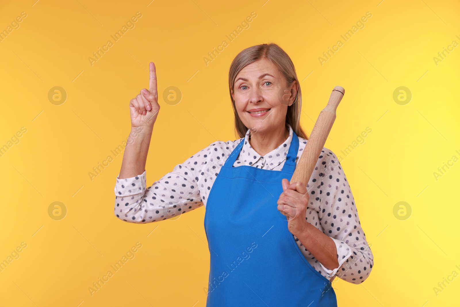 Photo of Happy woman with rolling pin pointing upwards on yellow background