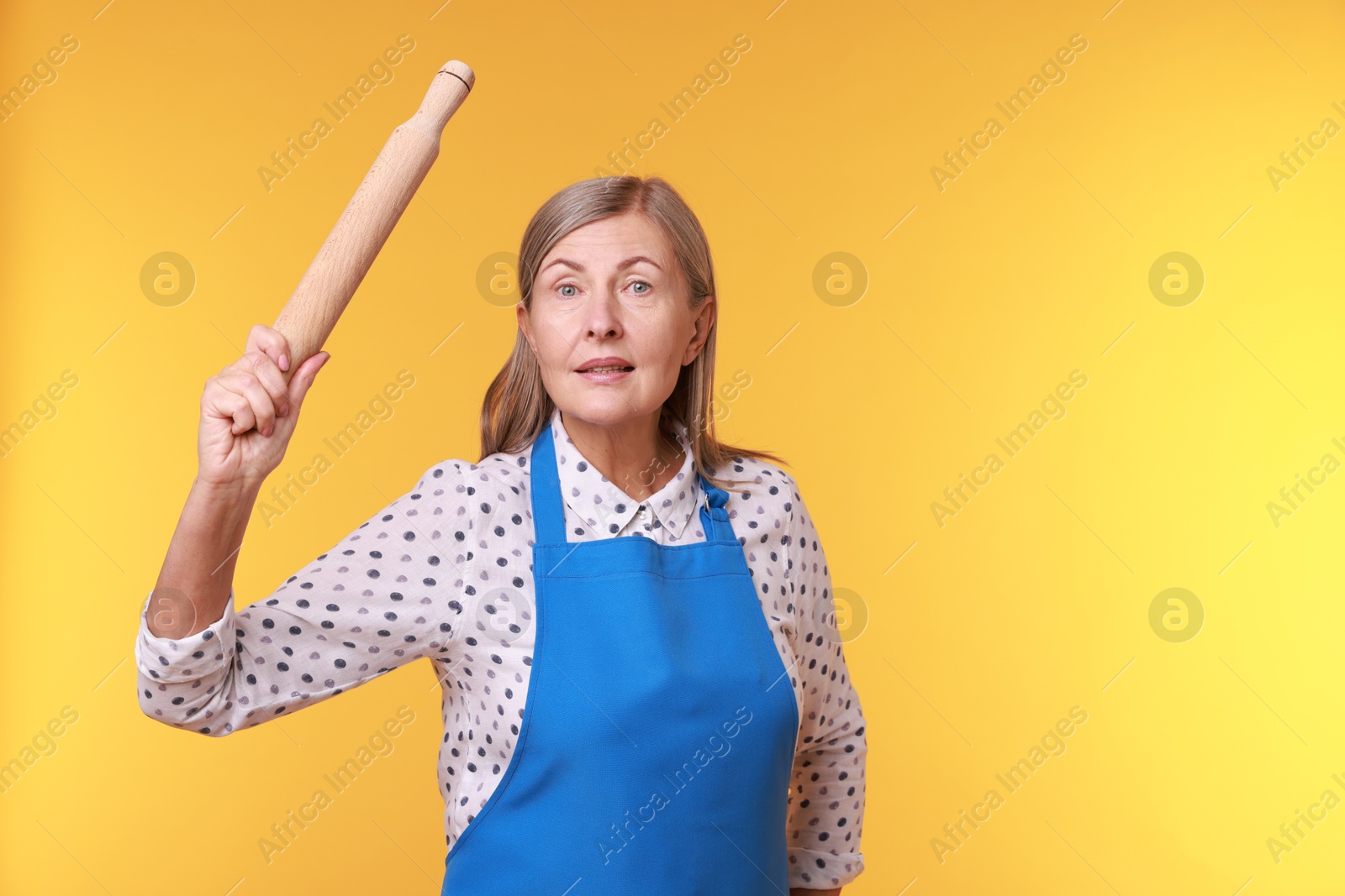 Photo of Emotional woman with rolling pin on yellow background. Space for text