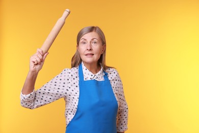 Photo of Emotional woman with rolling pin on yellow background. Space for text