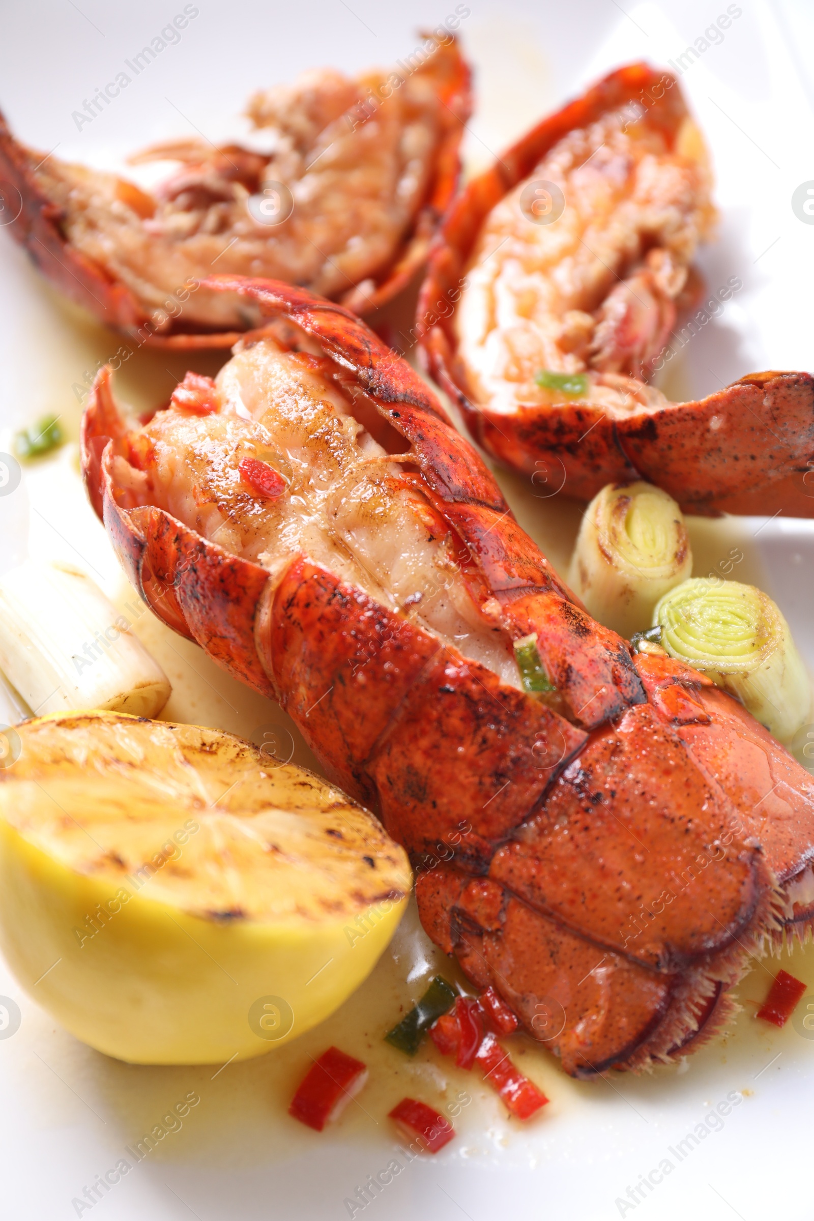 Photo of Delicious lobster tails with lemon and green onion on white plate, closeup