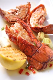 Delicious lobster tails with lemon and green onion on white plate, closeup