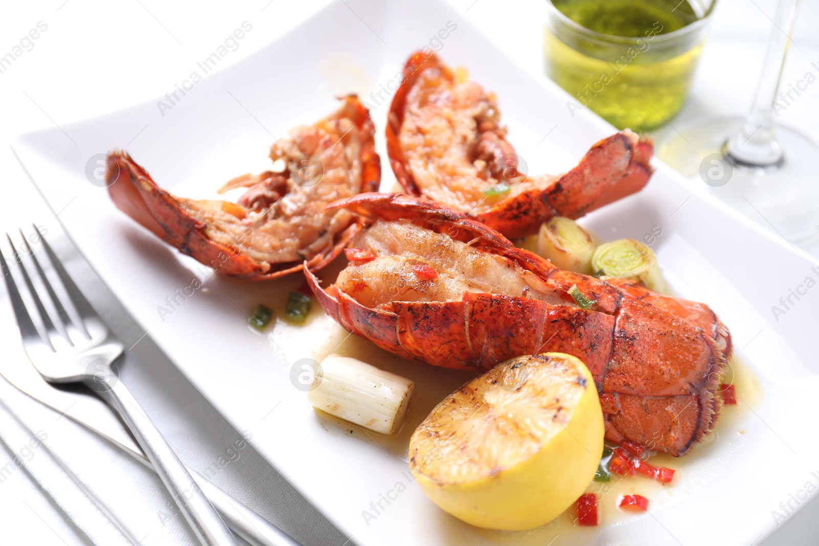 Photo of Delicious lobster tails with lemon and green onion on white table, closeup