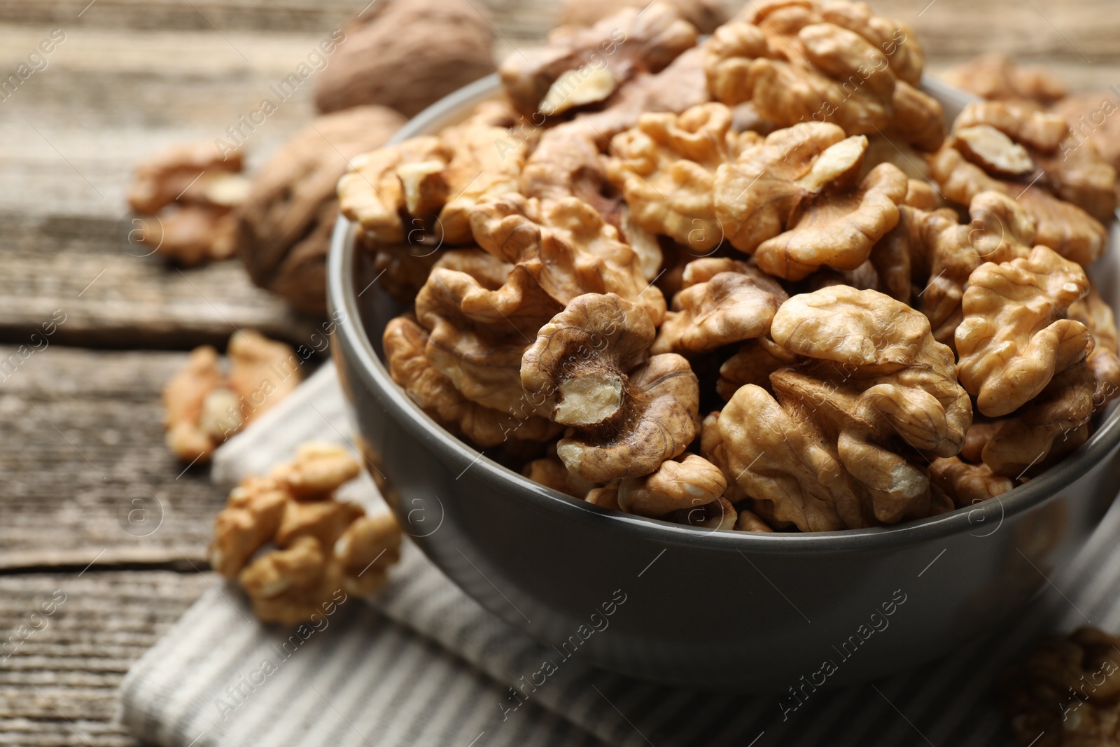 Photo of Fresh walnuts in bowl on wooden table, closeup