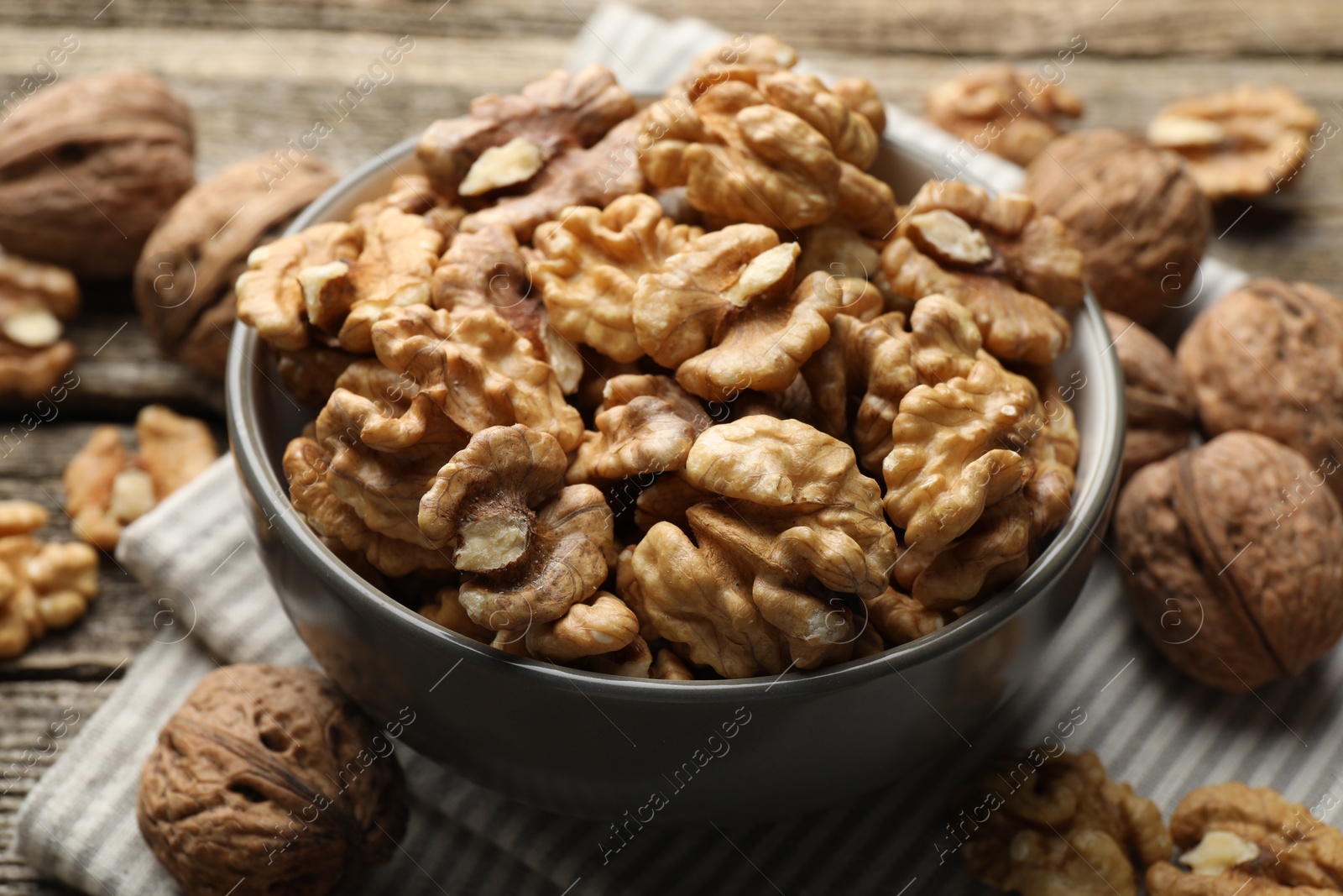 Photo of Shelled walnuts in bowl and whole ones on table, closeup