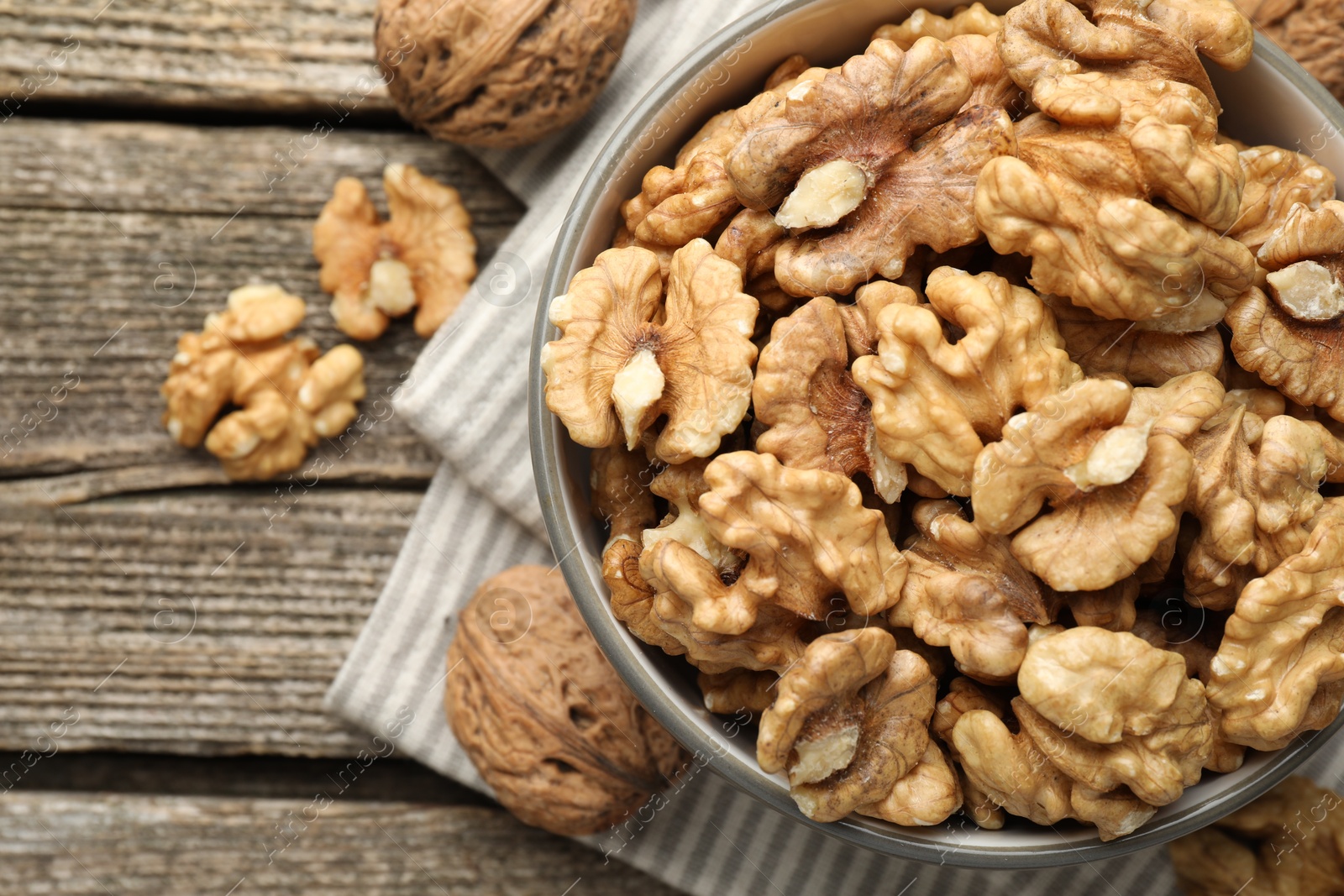 Photo of Shelled walnuts in bowl and whole ones on wooden table, flat lay