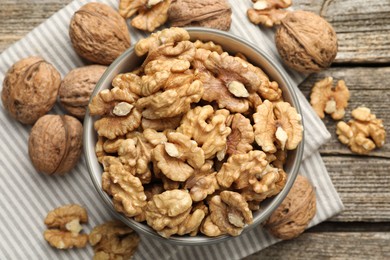 Photo of Shelled walnuts in bowl and whole ones on wooden table, flat lay