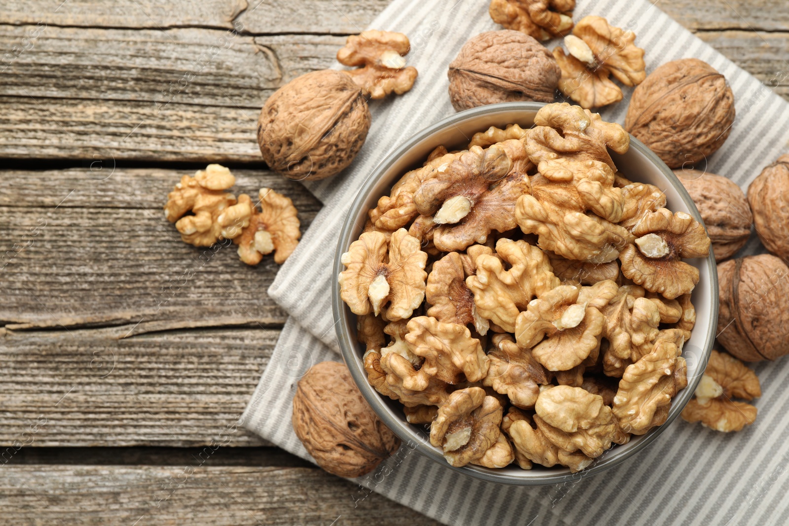 Photo of Shelled walnuts in bowl and whole ones on wooden table, flat lay. Space for text