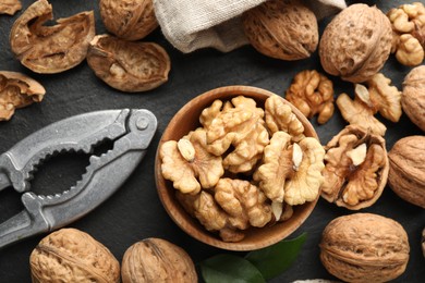 Photo of Fresh ripe walnuts, shells and nutcracker on black table, flat lay