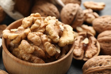 Photo of Shelled walnuts in bowl and whole ones on table, closeup