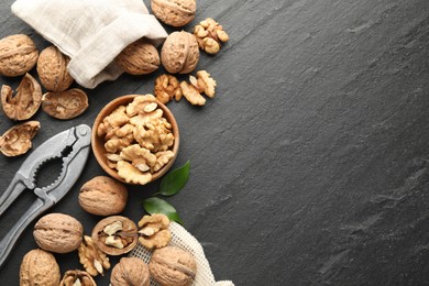 Photo of Fresh ripe walnuts, shells and nutcracker on black table, flat lay. Space for text