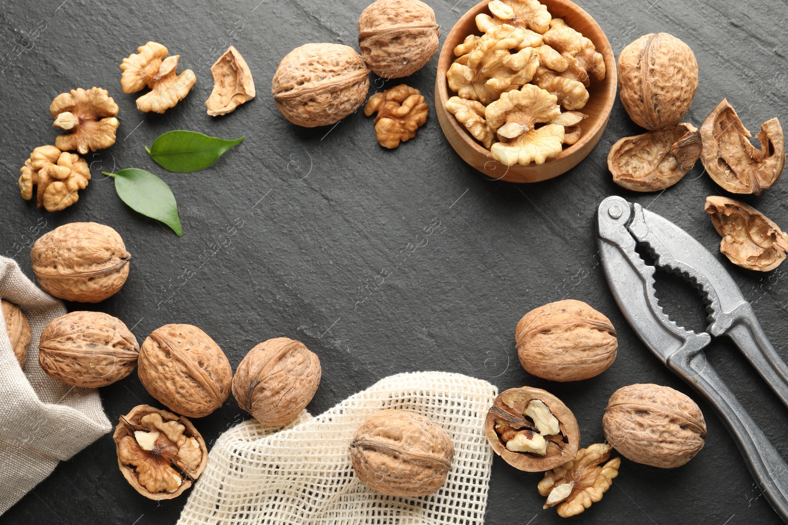 Photo of Frame of fresh ripe walnuts, shells and nutcracker on black table, flat lay