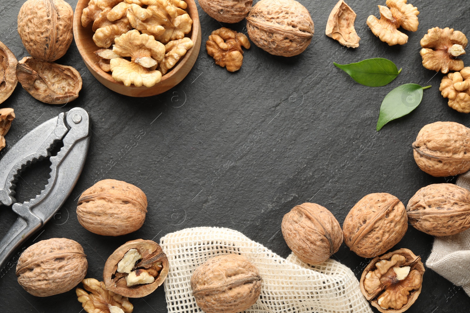 Photo of Frame of fresh ripe walnuts, shells and nutcracker on black table, flat lay