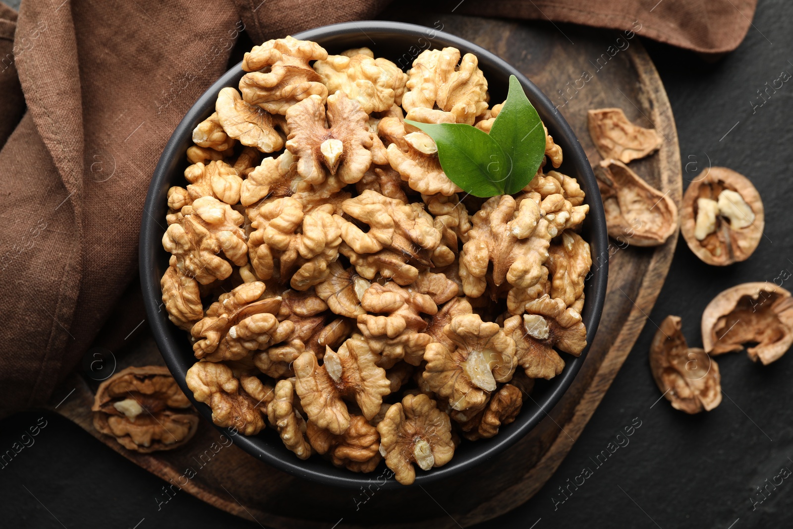 Photo of Fresh ripe walnuts in bowl and shells on black table, top view