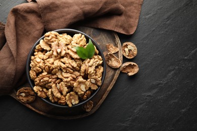 Photo of Fresh ripe walnuts in bowl and shells on black table, top view. Space for text