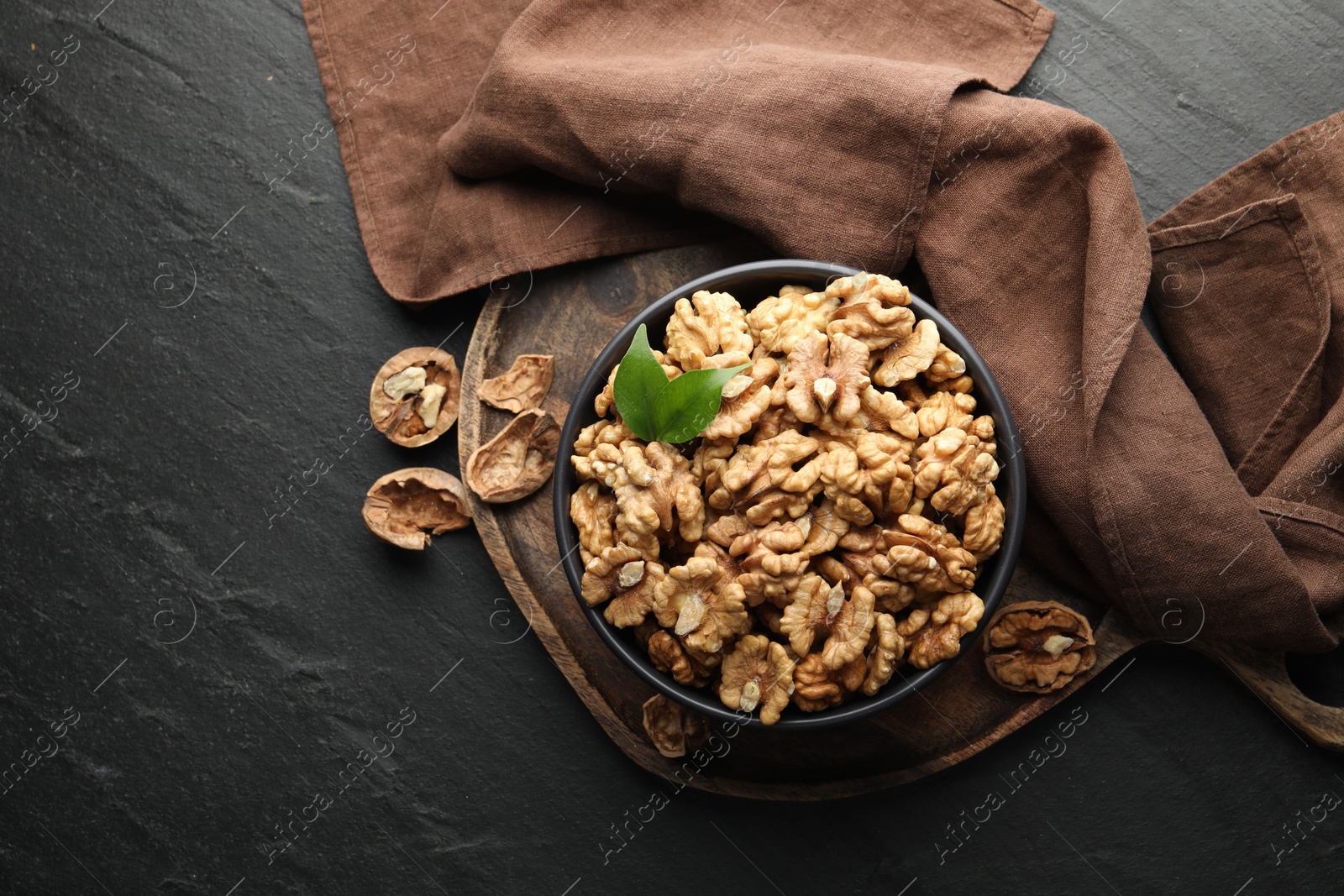 Photo of Fresh ripe walnuts in bowl and shells on black table, top view. Space for text