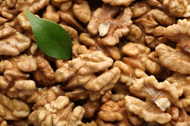 Photo of Pile of fresh ripe walnuts and green leaves as background, top view