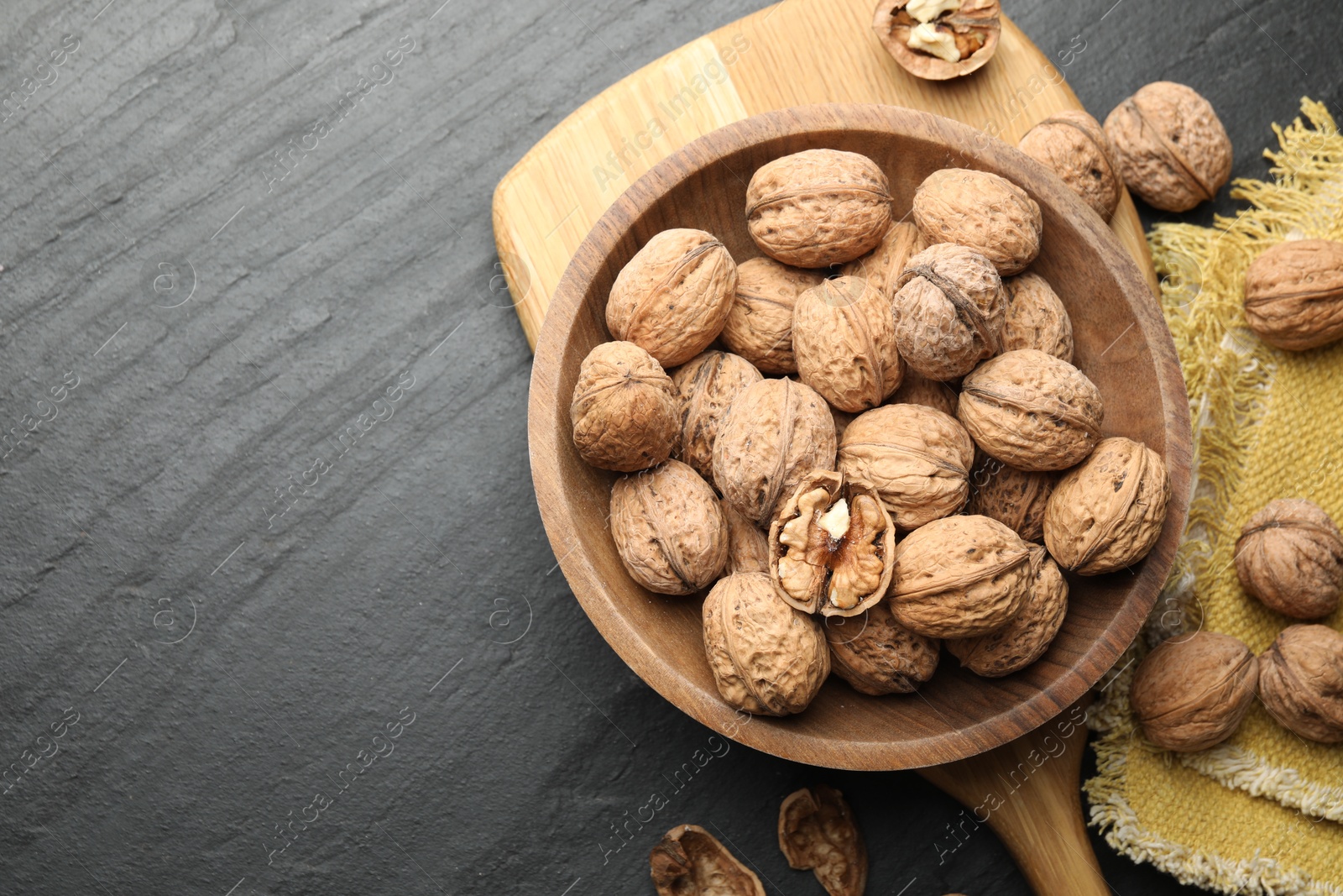 Photo of Fresh ripe walnuts in shells on black table, flat lay. Space for text