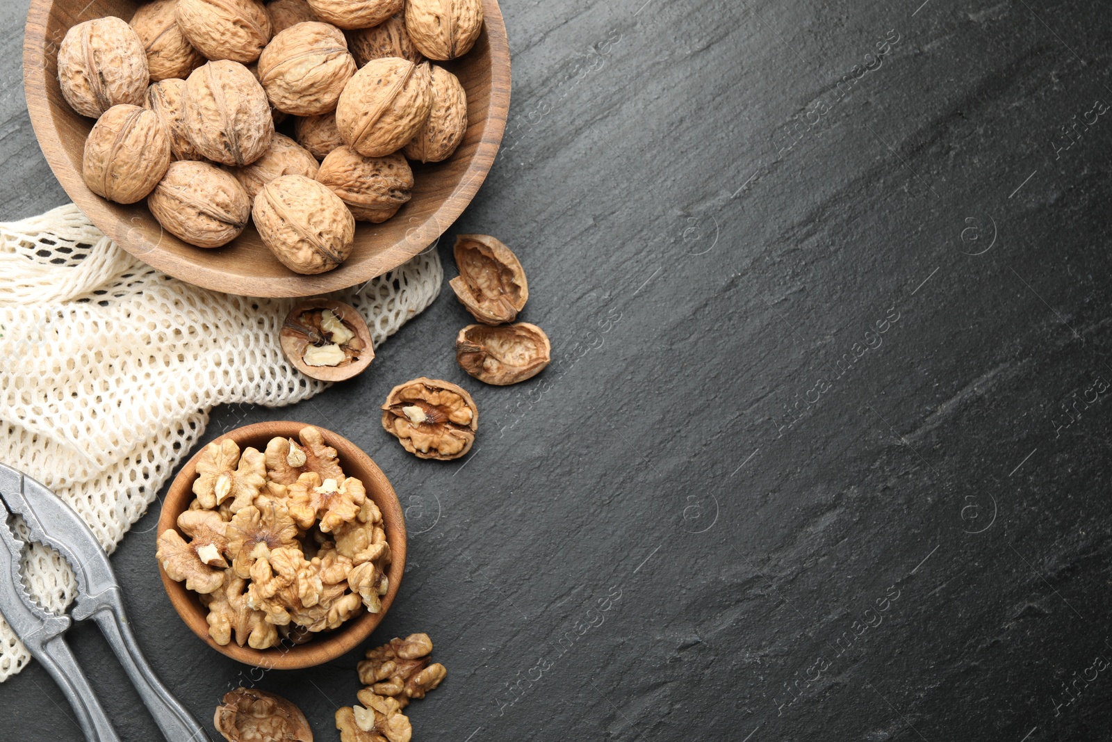 Photo of Fresh ripe walnuts, nutcracker and shells on black table, flat lay. Space for text