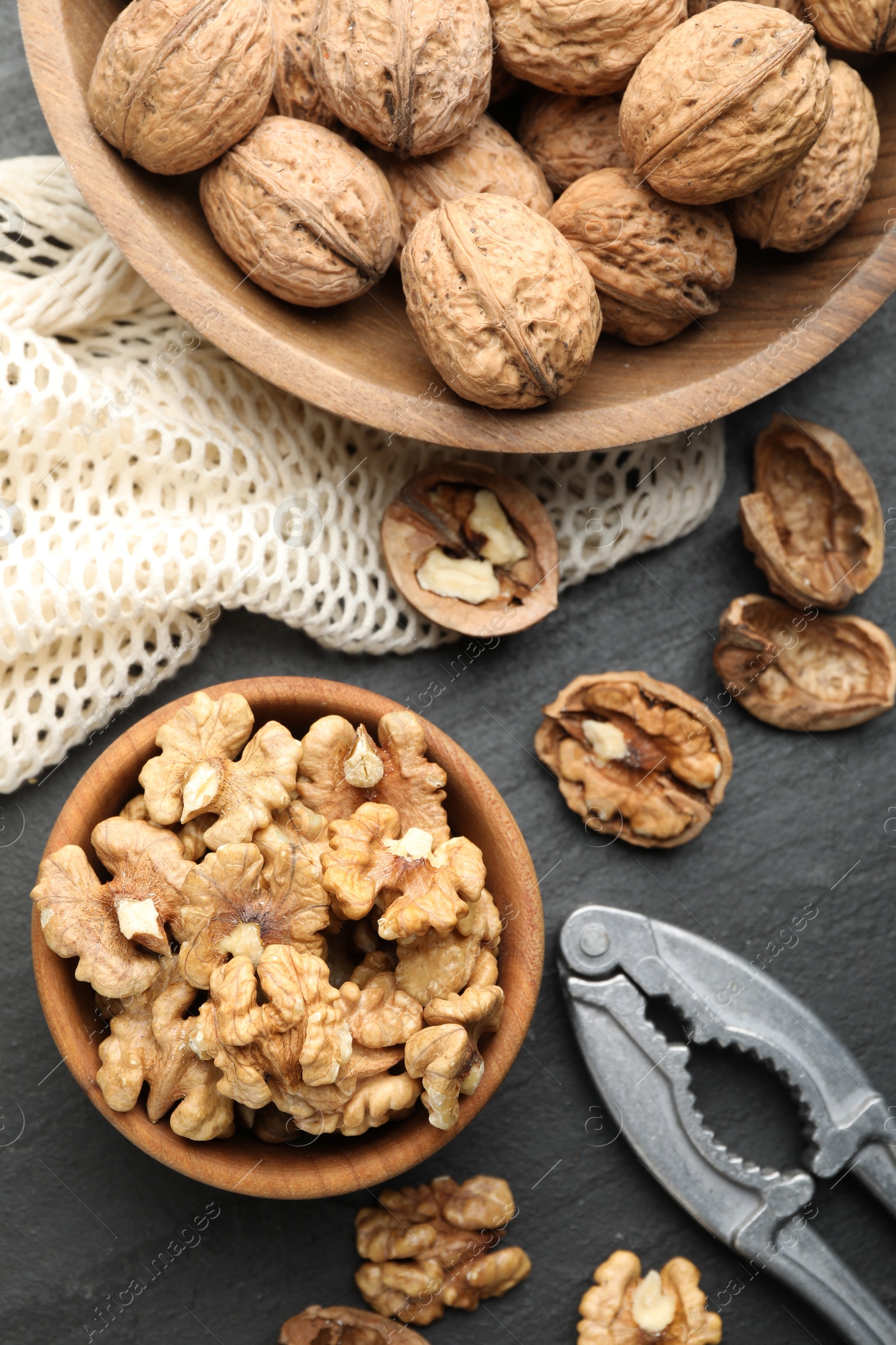 Photo of Fresh ripe walnuts, nutcracker and shells on black table, flat lay