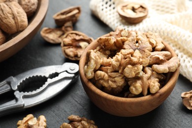 Photo of Fresh ripe walnuts in bowl and nutcracker on black table, closeup